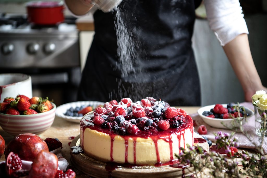 Berry-topped cheesecake being finished with icing sugar